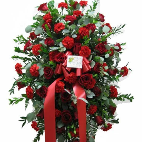 Tall standing spray of red roses and carnations with a red ribbon on an easel