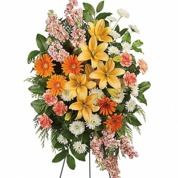 Tall standing spray of yellow lilies, orange gerberas, white mums, and peach flowers on a metal easel
