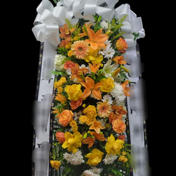 Tall standing floral spray with orange and yellow blooms and a large white bow