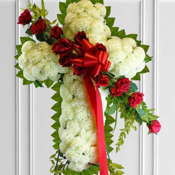 Cross-shaped floral spray with white blooms, red roses, and a red ribbon