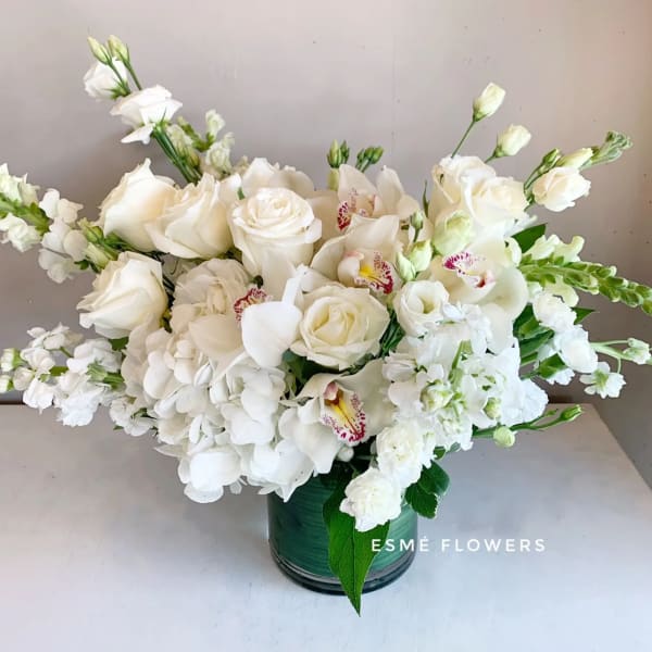 White floral arrangement in a green vase with roses and orchids