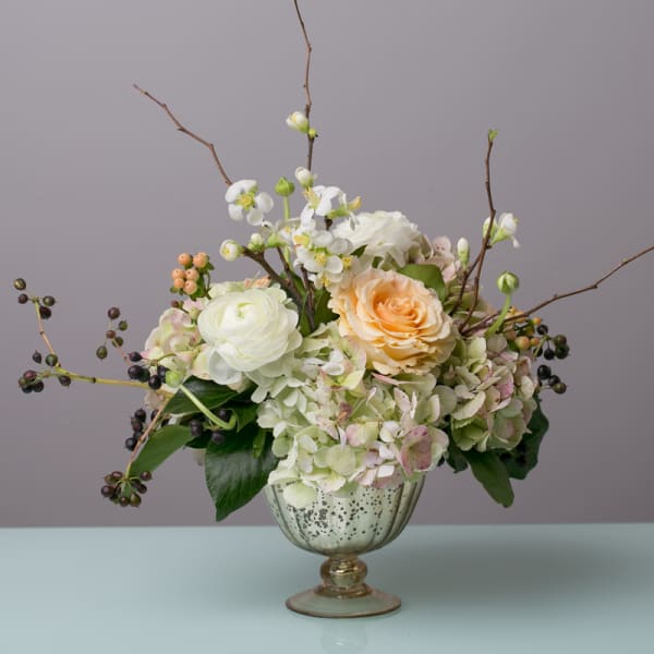 Mixed white and peach flowers arranged in a glass pedestal vase