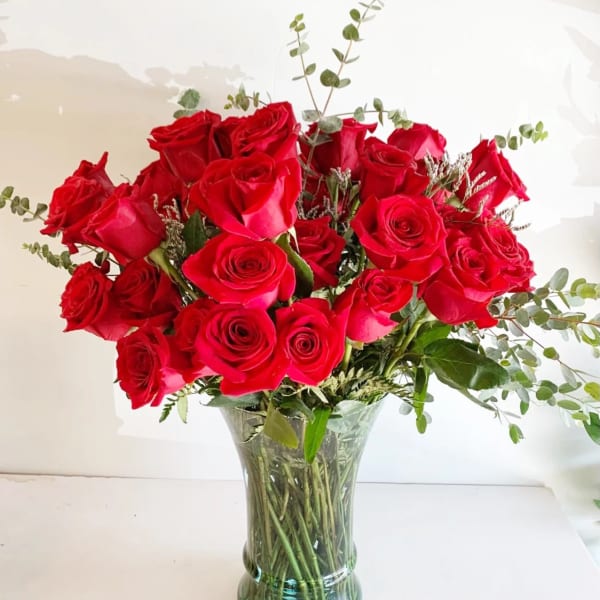 Red roses arranged in a clear glass vase with airy greenery
