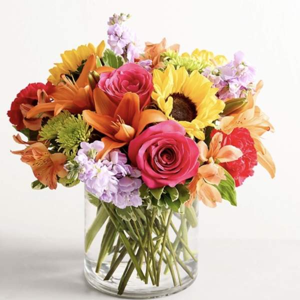 Mixed bouquet of roses, sunflowers, lilies, and carnations in a glass vase