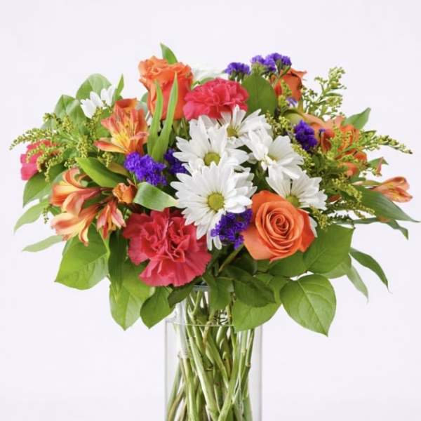 Mixed bouquet of orange, pink, and white flowers in a clear glass vase