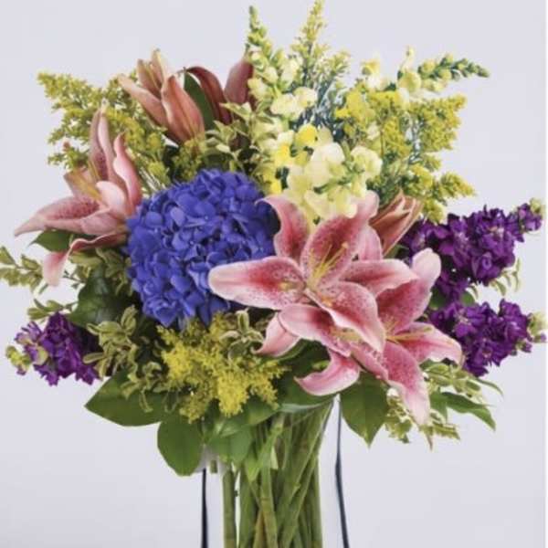 Bouquet of pink lilies, blue hydrangea, and purple flowers in a clear glass vase