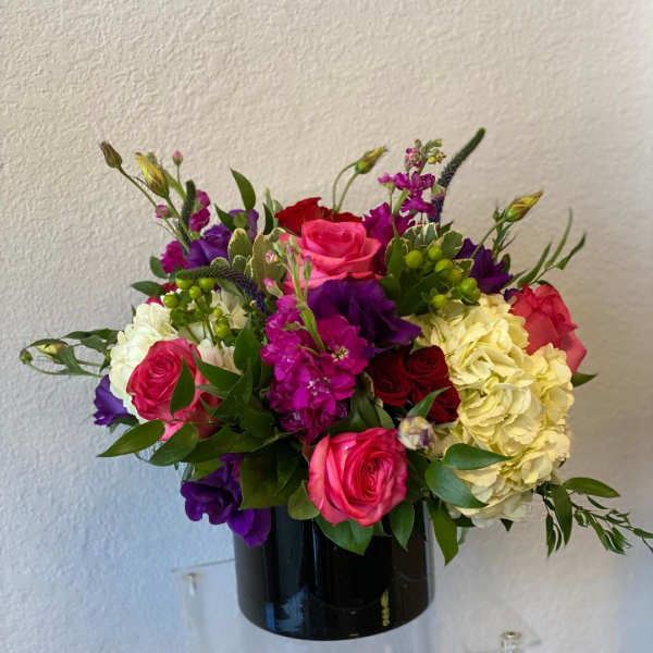 Mixed bouquet of roses, hydrangeas, and purple blooms in a black vase