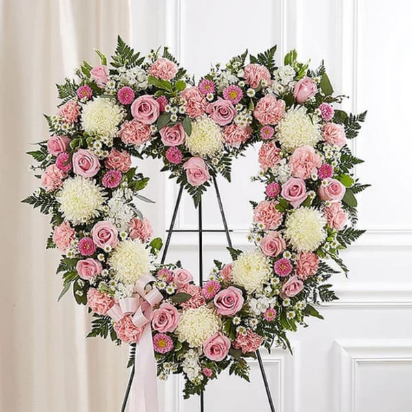 Heart-shaped floral wreath with pink roses and white blooms on a stand