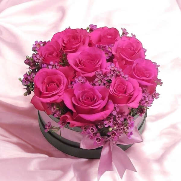 Pink roses arranged in a round hatbox with a ribbon