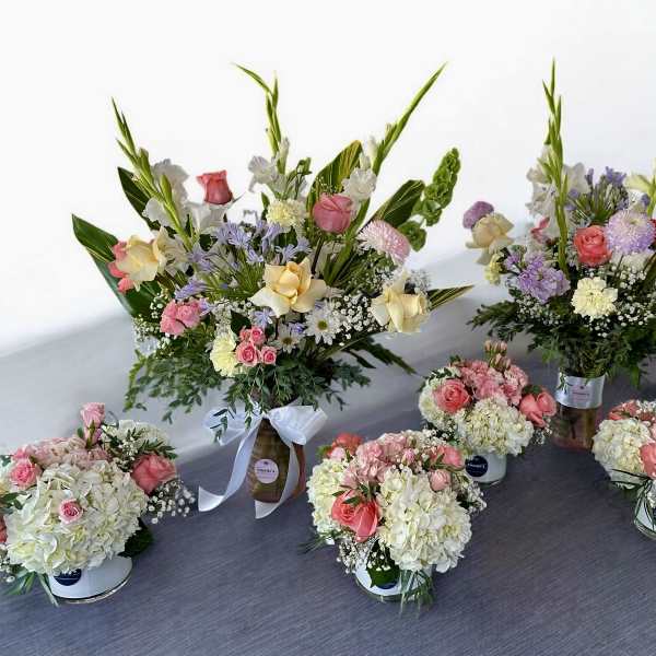 Assorted floral arrangements with pink and cream roses in containers