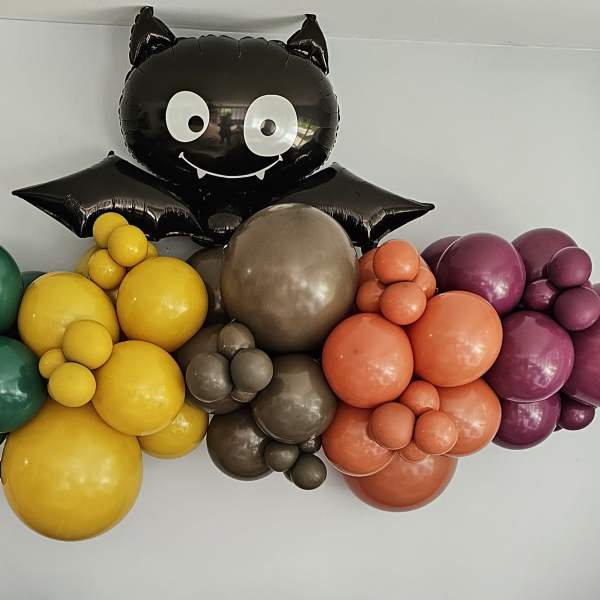 Black cat balloon above a colorful balloon garland on a wall