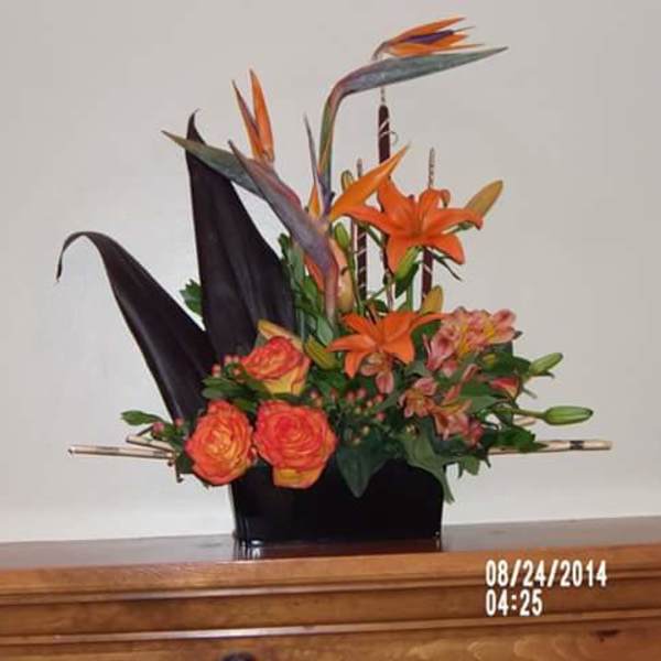 Orange lilies and roses in a black vase with tall dark leaves