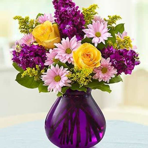 Yellow roses and pink daisies in a purple glass vase
