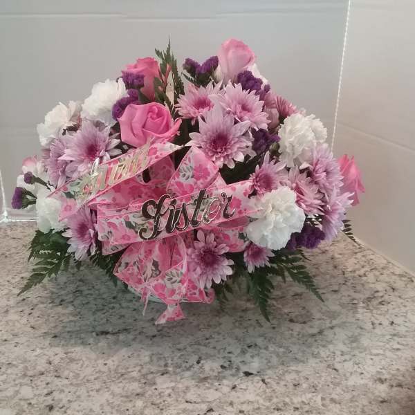 Pink and white floral arrangement with a pink ribbon and "sister" sign