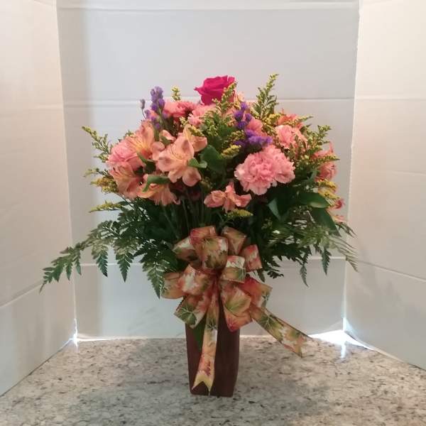Pink and peach mixed flower arrangement in a tall vase with a ribbon