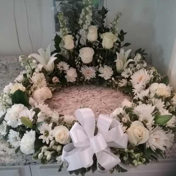 White floral wreath with roses, lilies, and daisies tied with a white bow