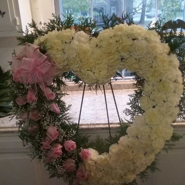 Heart-shaped floral wreath with white blooms and pink roses on an easel