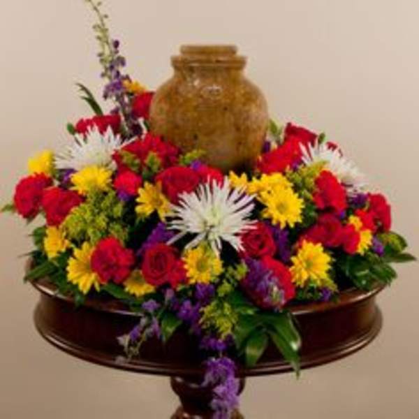 Colorful mixed flower arrangement around a brown urn on a pedestal