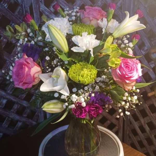 Mixed bouquet of pink roses, white lilies, and chrysanthemums in a glass vase