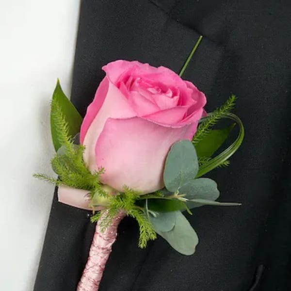 Pink rose boutonniere with green foliage on a black suit