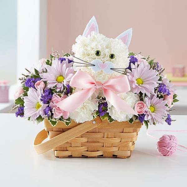 White cat-shaped flower arrangement in a wicker basket with pink and purple flowers