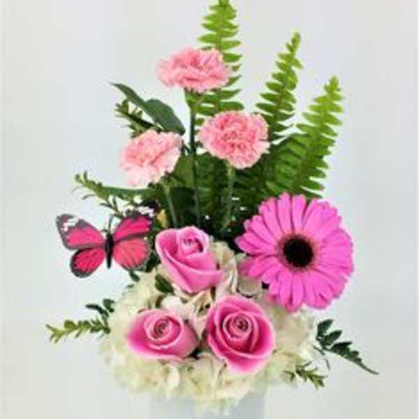 Pink roses and carnations in a white vase with a butterfly accent