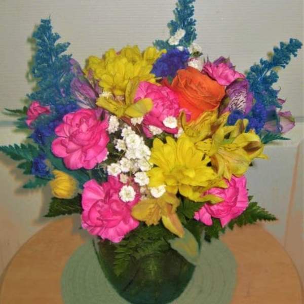 Bright mixed bouquet in a green vase with pink, yellow, orange, and blue flowers