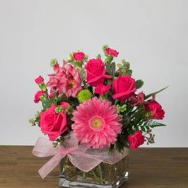 Pink mixed flower arrangement in a square glass vase with a ribbon