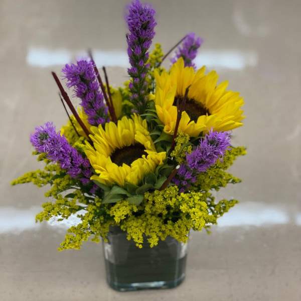 Sunflowers and purple flowers arranged in a square glass vase
