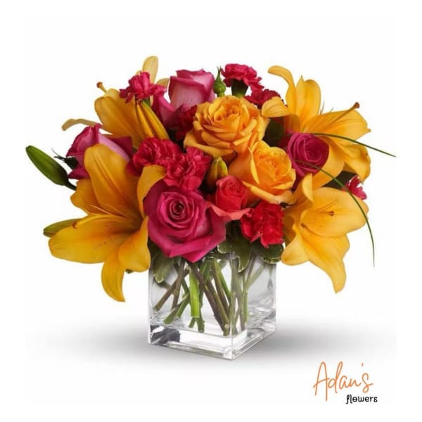 Bouquet of yellow lilies, pink roses, and red carnations in a clear glass vase