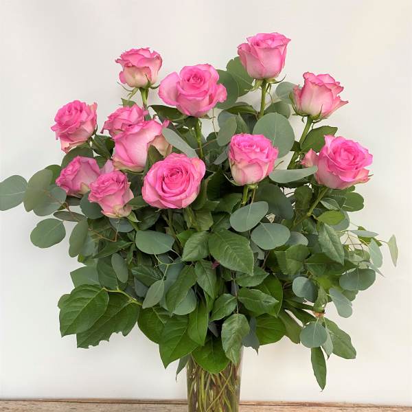 Pink roses arranged in a clear glass vase with eucalyptus foliage