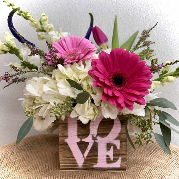 Pink and white flowers arranged in a wooden box with the word LOVE.