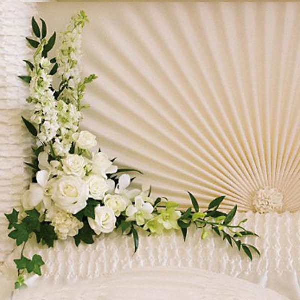 Corner arrangement of white roses and other white flowers with trailing greenery on a textured cream backdrop
