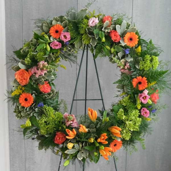 Large floral wreath with orange, pink, and green flowers on a black stand