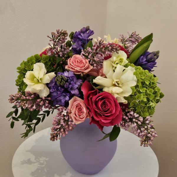 Mixed bouquet of roses, hyacinths, and hydrangeas in a lavender vase