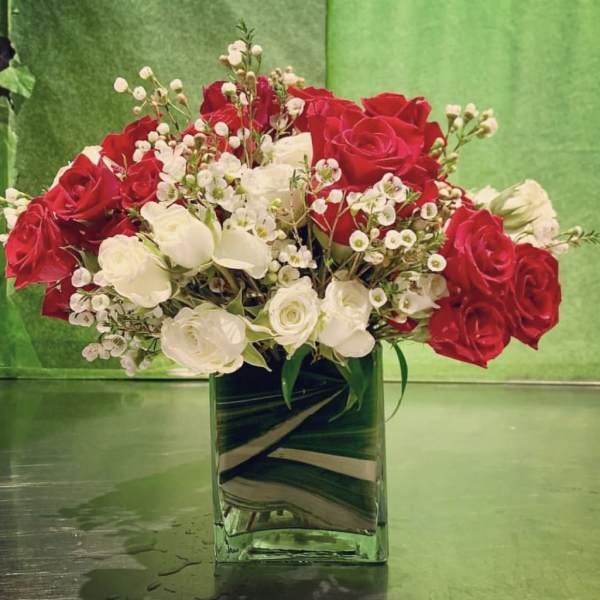 Red and white roses arranged in a square glass vase.
