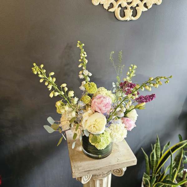 Tall pastel flower arrangement in a glass vase on a pedestal