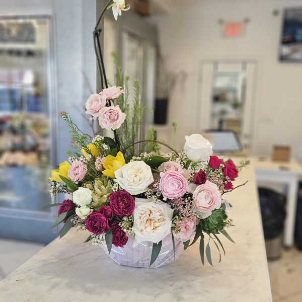 Mixed pink, white, and yellow roses in a low arrangement with a tall white orchid stem