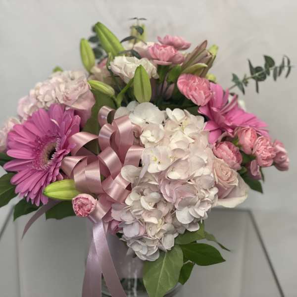 Pink and white bouquet with lilies, hydrangeas, and a ribbon in a vase