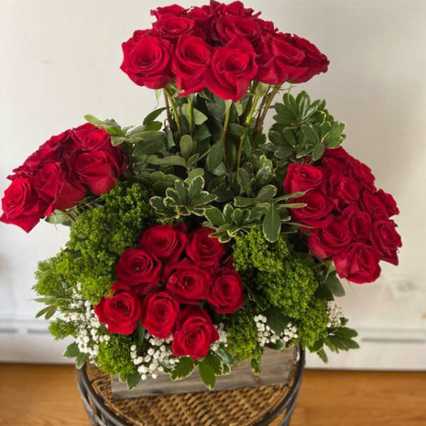 Tiered arrangement of red roses with greenery in a basket container