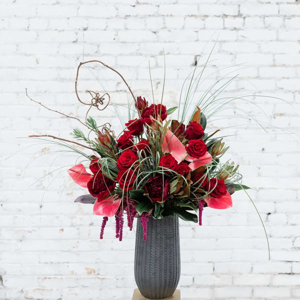 Tall red floral arrangement in a dark vase on a stand