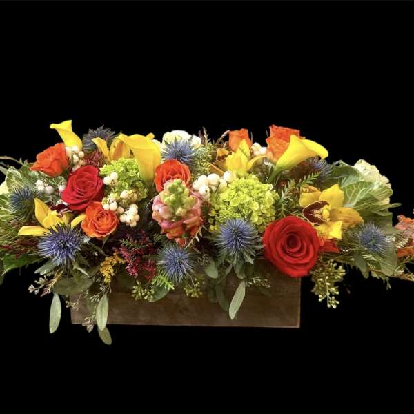 Long floral arrangement in a wooden box with red, yellow, and orange blooms
