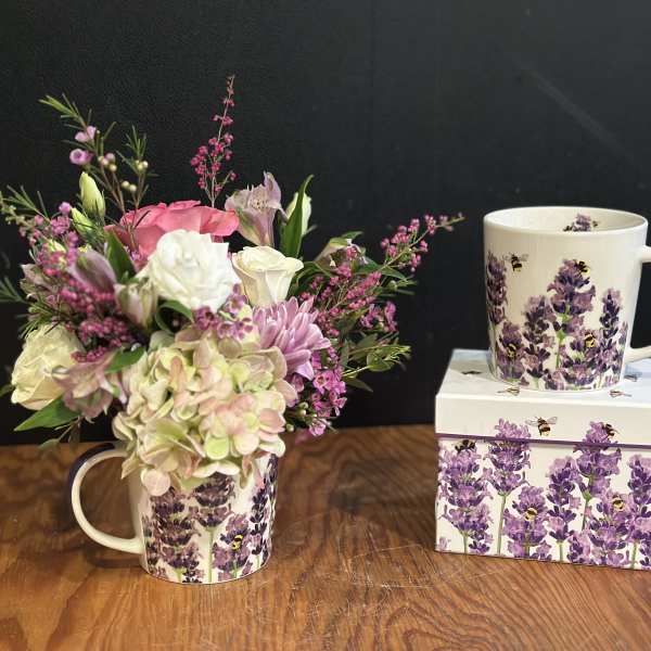 Pink and white flower arrangement in a lavender bee-patterned mug beside a matching mug and box