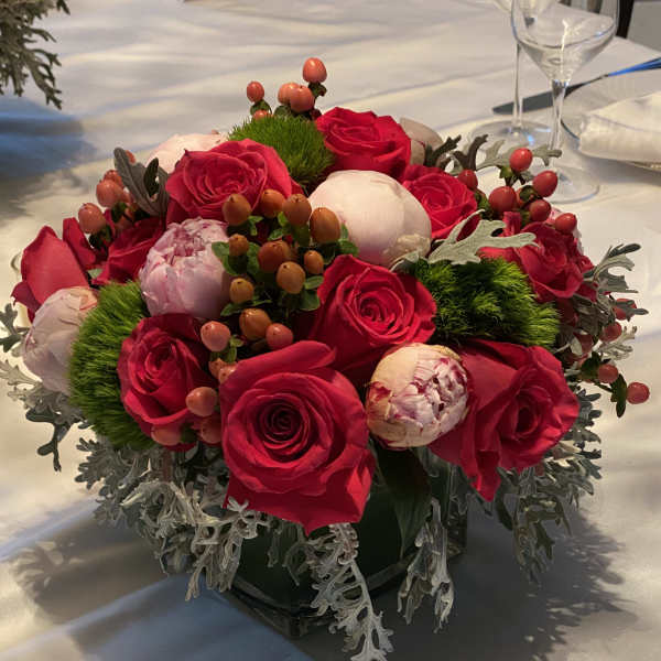 Compact arrangement of red roses and pale peonies in a low vase