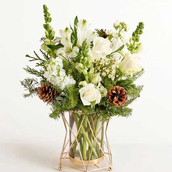 White floral arrangement in a gold geometric vase with pinecones