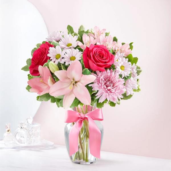Pink and white mixed flower bouquet in a glass vase with a pink ribbon