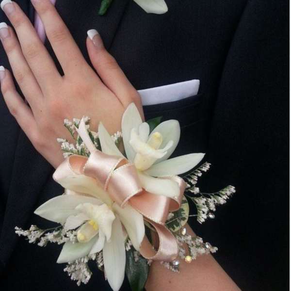 White floral corsage and boutonniere on a black suit with pink ribbon