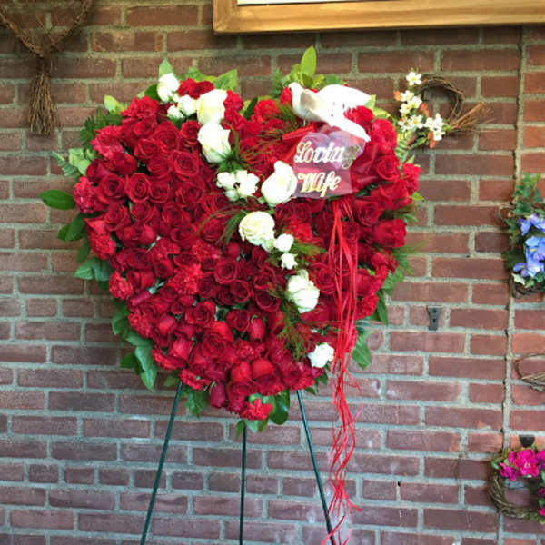 Heart-shaped red rose arrangement with white roses and a ribbon on an easel