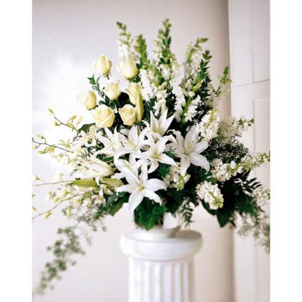 Tall white arrangement of lilies and roses in a white urn on a pedestal