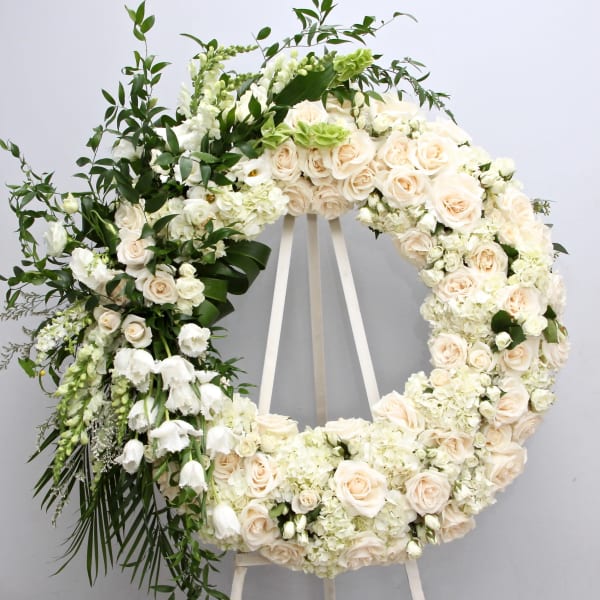 Large white floral wreath on an easel with cream roses and greenery